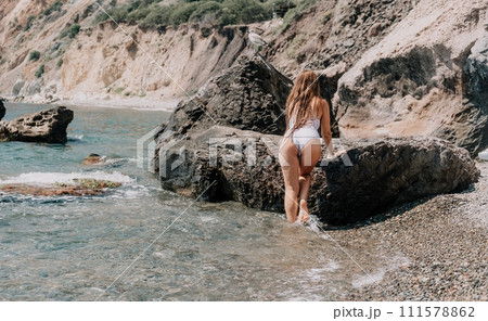 Woman travel sea. Happy tourist in white bikini enjoy taking picture outdoors for memories. Woman traveler posing on the beach at sea surrounded by volcanic mountains, sharing travel adventure journey 111578862