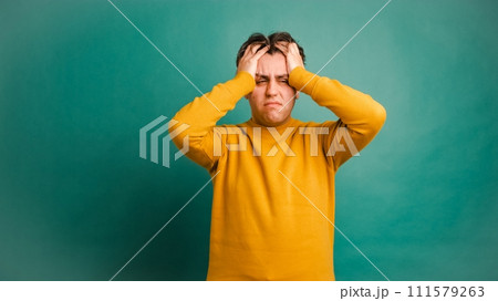Frustrated man suffering from headache in green studio Frustrated man suffering from headache in green studio 111579263