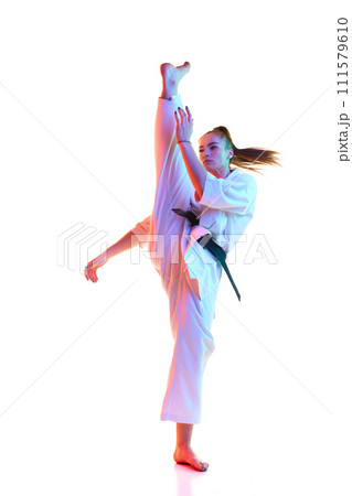 Portrait of young woman, female fighter in uniform with black belt training high kick isolated over white studio background. Portrait of young woman, female fighter in uniform with black belt training high kick isolated over white studio background. 111579610
