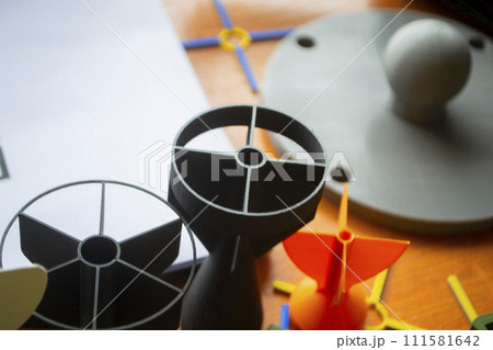 Prototype model of rocket bomb tip printed on 3D printer. Small colored models of tail fins, tail cone printed on 3D printer from molten plastic on table. New modern innovation printing technology 111581642