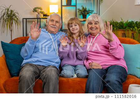 Child girl granddaughter with grandparents bloggers waves hand hello hi relaxing making on home sofa 111582016