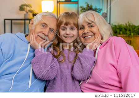 Portrait of smiling kid granddaughter and loving grandfather and grandmother looking at camera home 111582017