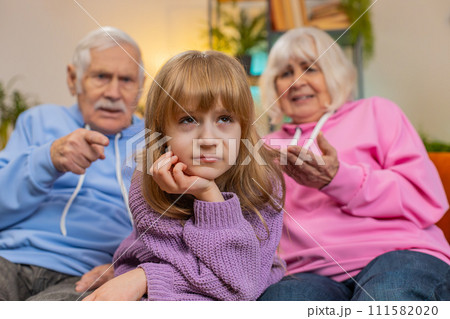 Irritated grandfather and grandmother scolding granddaughter child kid for bad behavior on home sofa Irritated grandfather and grandmother scolding granddaughter child kid for bad behavior on home sofa 111582020