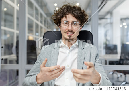 A young mature businessman with curly hair engages in conversation at his office, exemplifying professionalism and confidence. 111583248