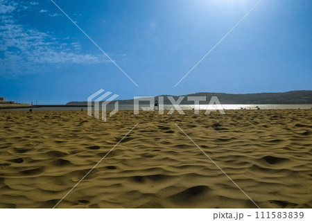 View of sand surface against blue sky background, with clouds, sun halo, reflection on ocean water. Unique natural areas, beaches, deserts. Place where all elements of Nature interact with each other 111583839
