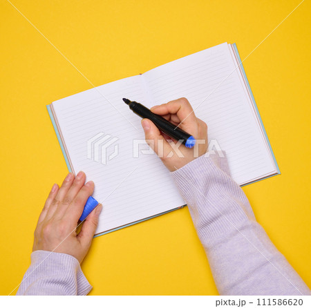 An open notebook with empty white sheets and a woman's hand holding a felt-tip pen on a yellow background An open notebook with empty white sheets and a woman's hand holding a felt-tip pen on a yellow background 111586620