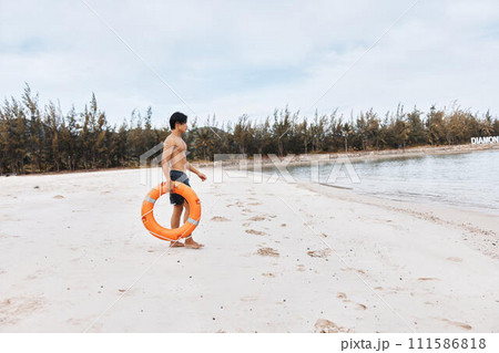 Beach Lifeguard: An Asian Man, the Rescuer of Summer, Embracing Safety and Joy amidst the Blue Ocean waves. 111586818