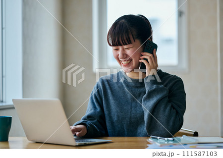 パソコンをタイピングしながら電話をする若い女性 111587103