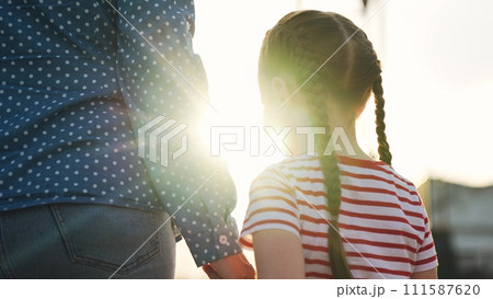 Smiling cute baby daughter and caring mother walking together holding hands summer park sun light back view closeup. Happy family woman and girl female kid child relaxing enjoy weekend outdoor Smiling cute baby daughter and caring mother walking together holding hands summer park sun light back view closeup. Happy family woman and girl female kid child relaxing enjoy weekend outdoor 111587620