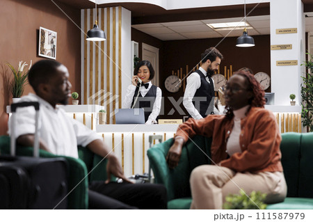 Employees working at front desk in hotel lobby, checking records and room availability at reception. Two receptionists answering landline phone call to make online reservations. Employees working at front desk in hotel lobby, checking records and room availability at reception. Two receptionists answering landline phone call to make online reservations. 111587979
