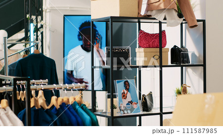 Modern boutique filled with trendy accessories, multiple racks with fashionable merchandise. Interior of empty clothing store with stylish clothes on hangers, small business concept. 111587985