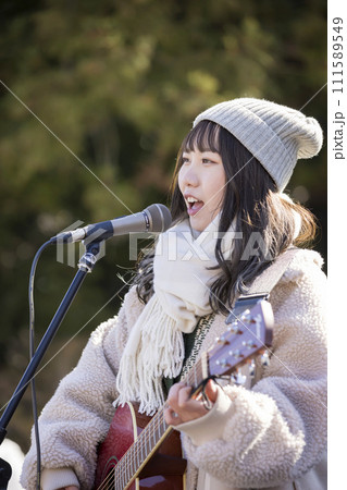 冬に弾き語りで路上ライブをする若い女性 111589549