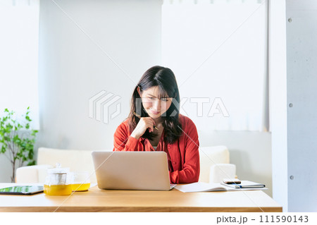 自宅のソファー前のローテーブルのノートパソコンで休日にオンライン講座を受講する30代の1人の女性 111590143