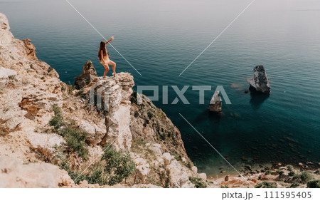 Woman travel sea. Happy tourist enjoy taking picture outdoors for memories. Woman traveler looks at the edge of the cliff on the sea bay of mountains, sharing travel adventure journey Woman travel sea. Happy tourist enjoy taking picture outdoors for memories. Woman traveler looks at the edge of the cliff on the sea bay of mountains, sharing travel adventure journey 111595405