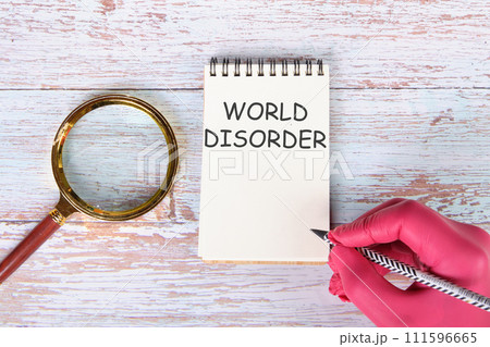 World Disorder writing on a notebook lying on old boards next to a magnifying glass and a hand in a red medical glove with a pencil 111596665