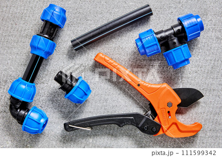 Assembly of outdoor water supply for drinking water and irrigation, compression fittings for plastic pipes laid out on gray surface next to ratchet pipe cutter. 111599342