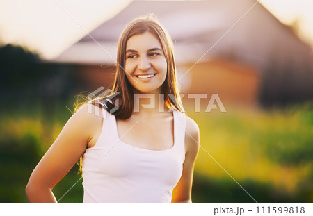 Perfect smile of young Caucasian woman with perfect teeth at setting sun against blurred background of rural landscape. 111599818