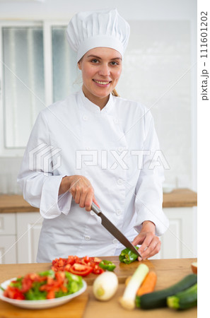 Proffesional woman cook in white uniform chopping vegetables 111601202