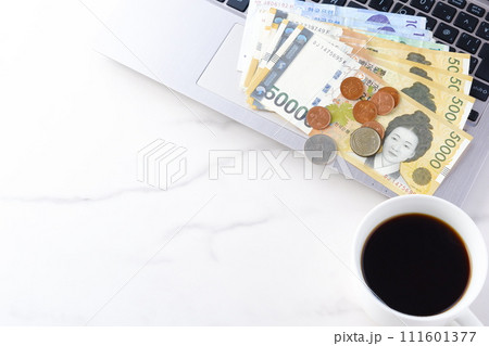 韓国の通貨、ウォンKRW（紙幣と硬貨）とノートパソコン、コーヒーの入ったコーヒーカップ 111601377