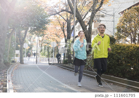 秋冬に公園をジョギングする男女の全身の広角写真 秋冬に公園をジョギングする男女の全身の広角写真 111601705