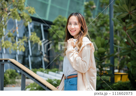 A city portrait of a cheerful Asian woman holding headphones embodies the modern joys of music communication and carefree happiness. A city portrait of a cheerful Asian woman holding headphones embodies the modern joys of music communication and carefree happiness. 111602073