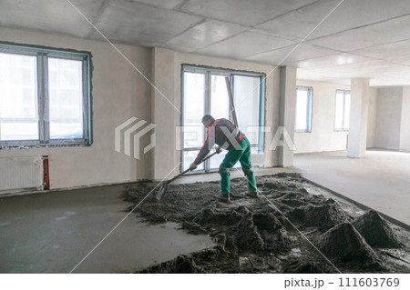 A builder in work clothes is doing his job, leveling the floor, pouring mortar 111603769