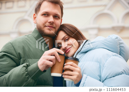 Lovely couple, young man and woman hugs and drinking coffee together while walking outdoor. First date. 111604453