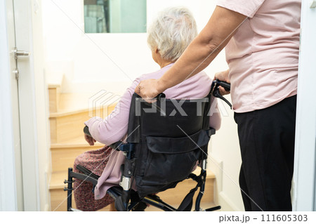 Caregiver help asian or elderly old woman sitting wheelchair support up the stairs in home. 111605303