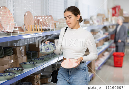 Young woman in supermarket is choosing plates with Asian pattern Young woman in supermarket is choosing plates with Asian pattern 111606074