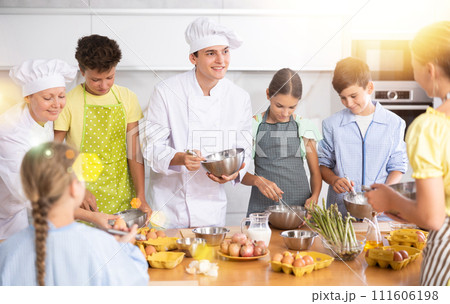 Young guy and adult woman cook teaches group of children to cook Young guy and adult woman cook teaches group of children to cook 111606198