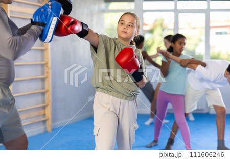 Preteen girl in boxing gloves practicing punches on mitts with coach Preteen girl in boxing gloves practicing punches on mitts with coach 111606246