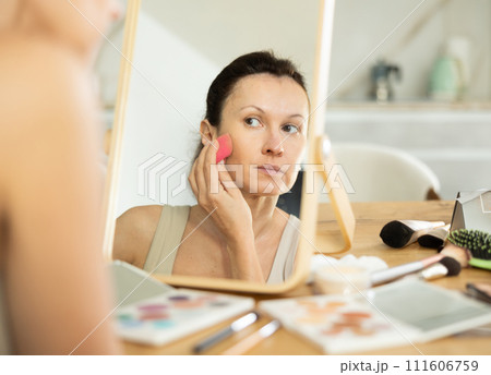 Woman applying foundation with makeup sponge in front of mirror 111606759