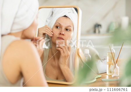 Middle-aged woman examining her facial skin looking in the mirror put on the table Middle-aged woman examining her facial skin looking in the mirror put on the table 111606761