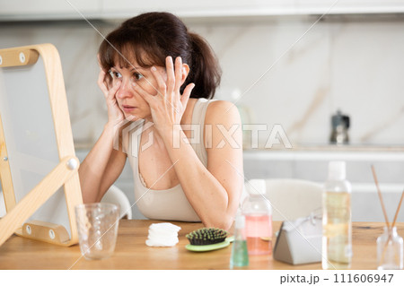 Woman inspecting facial skin in mirror during daily routine Woman inspecting facial skin in mirror during daily routine 111606947