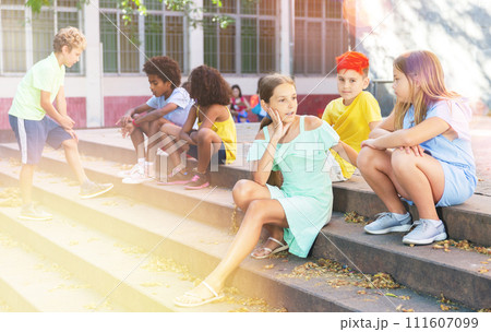 Group of kids sitting on stairs outdoors and talking 111607099