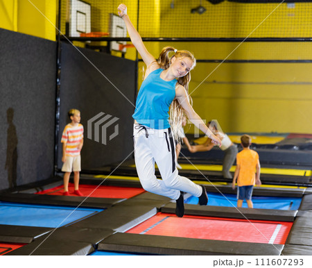 Happy teen girl in blue jersey and white pants jumping and indulging on trampolines in entertainment center 111607293