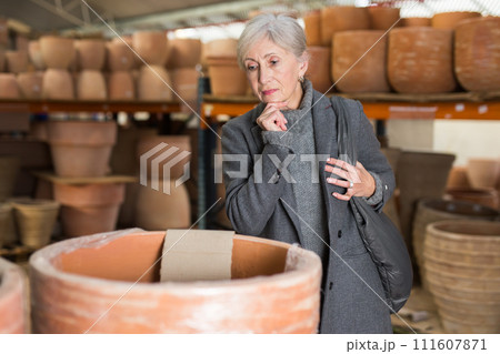 Senior woman looking for pots for growing plants in greenhouse 111607871