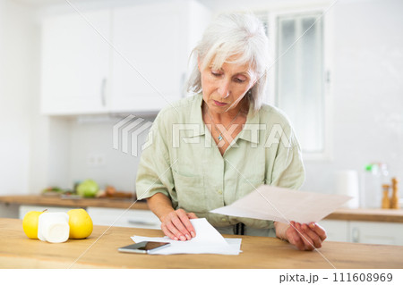 Senior woman working with papers at kitchen Senior woman working with papers at kitchen 111608969