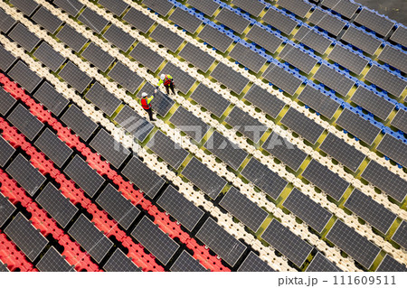 Wide shot of aeroview or top view of two technician workers discuss and work with maintenance or check solar panel system over water resirvoir for green ecosystem energy for good environment. 111609511