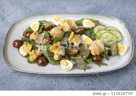 Warm salad with rapan (snails), tomatoes, cucumbers, leafy vegetables, quail eggs and olive oil. Traditional seafood salad. Close-up, selective focus. Warm salad with rapan (snails), tomatoes, cucumbers, leafy vegetables, quail eggs and olive oil. Traditional seafood salad. Close-up, selective focus. 111610750