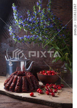 Delicious chocolate cake with sweet cherry, vintage kettle and bouquet of blue flowers on dark wooden background.. Delicious chocolate cake with sweet cherry, vintage kettle and bouquet of blue flowers on dark wooden background.. 111611267