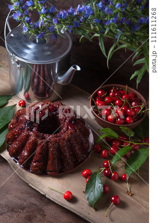 Delicious chocolate cake with berry of sweet cherry, vintage kettle and bouquet of blue flowers on dark wooden background.. Delicious chocolate cake with berry of sweet cherry, vintage kettle and bouquet of blue flowers on dark wooden background.. 111611268