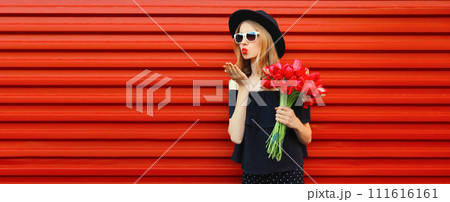 Beautiful stylish woman with bouquet of red rose flowers blowing kiss in black round hat 111616161