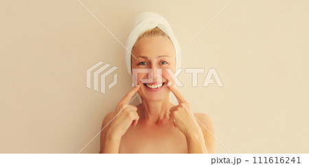 Happy smiling middle-aged woman points to her white clean teeth drying her wet hair Happy smiling middle-aged woman points to her white clean teeth drying her wet hair 111616241