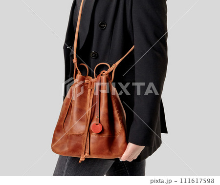 Stylish woman in black jacket holding brown leather drawstring bag 111617598
