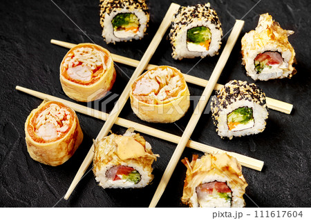 Sushi rolls and chopsticks arranged in tic-tac-toe game on black Sushi rolls and chopsticks arranged in tic-tac-toe game on black 111617604