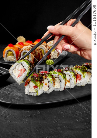 Female hand taking shrimp sushi roll from slate plate by chopsticks Female hand taking shrimp sushi roll from slate plate by chopsticks 111617609