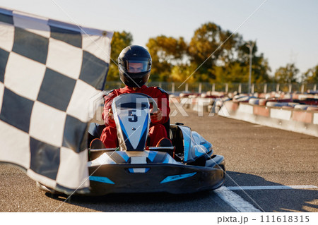 Go-kart driver crossing at finish line moving to checkered racing flag Go-kart driver crossing at finish line moving to checkered racing flag 111618315