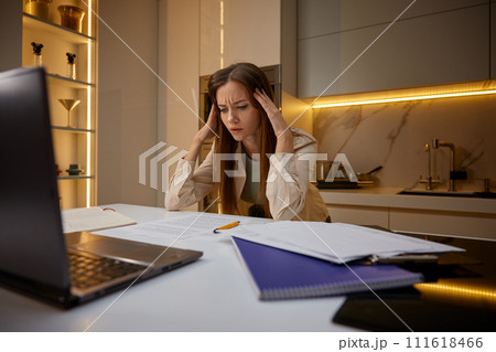 Overwhelmed woman touching head in panic sitting front of laptop at home 111618466