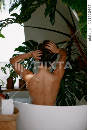 View from back on beautiful woman massaging neck while taking bath at home 111618497